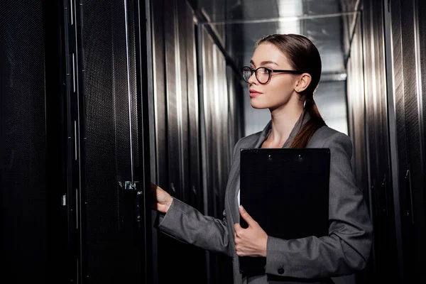 Beautiful businesswoman in glasses holding clipboard in data center — Stock Photo