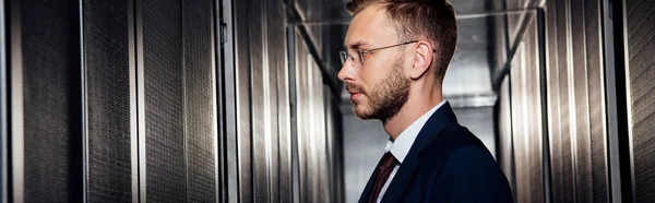 Panoramic shot of businessman in glasses near server racks in data center — Stock Photo