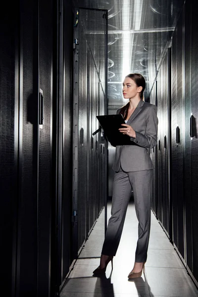 Hermosa mujer de negocios sosteniendo portapapeles mientras está de pie en el centro de datos - foto de stock