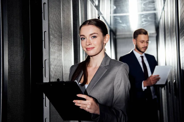 Selektiver Fokus einer fröhlichen Geschäftsfrau mit Klemmbrett in der Nähe eines bärtigen Geschäftsmannes im Datengalopp — Stockfoto