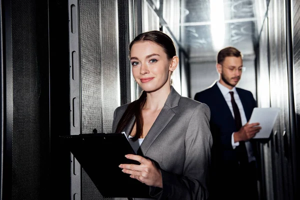 Foyer sélectif de femme d'affaires gaie tenant presse-papiers près de barbu homme d'affaires dans le canter de données — Photo de stock