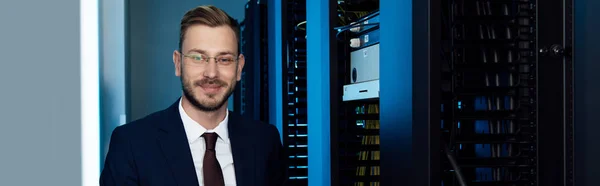 Tiro panorâmico de empresário em óculos sorrindo em data center — Fotografia de Stock