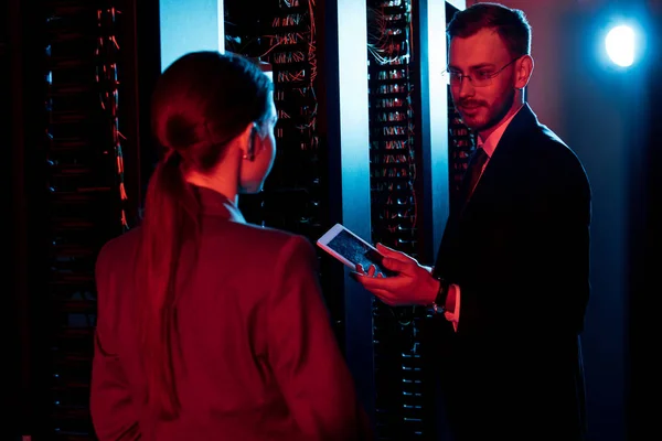 Selektiver Fokus eines gutaussehenden, bärtigen Geschäftsmannes mit digitalem Tablet in der Nähe einer Frau im Serverraum — Stockfoto