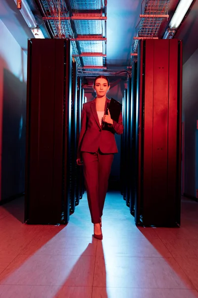 Attractive businesswoman holding clipboard while walking in server room — Stock Photo