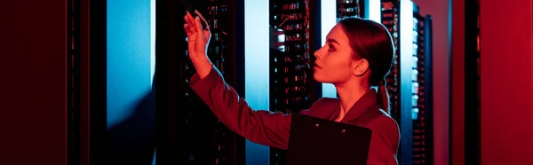 Panoramic shot of businesswoman holding clipboard and looking at server room — Stock Photo