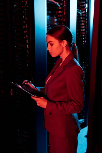 Seitenansicht einer Geschäftsfrau mit Klemmbrett im Serverraum — Stockfoto