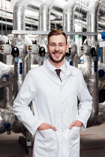 Ingénieur joyeux en manteau blanc debout avec les mains dans les poches — Photo de stock