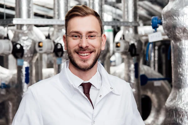 Fröhlicher Ingenieur mit Brille und weißem Mantel blickt in die Kamera — Stockfoto