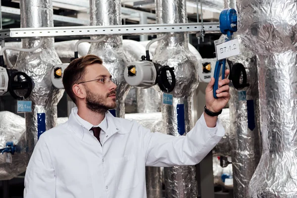 Bearded engineer in white coat checking compresses air system — Stock Photo