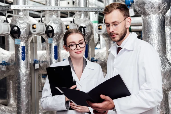 Engineers in white coats looking at folder near compressed air system — Stock Photo