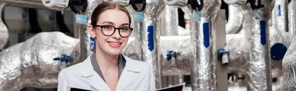 Panoramic shot of happy and attractive engineer in white coat near air compressed system — Stock Photo