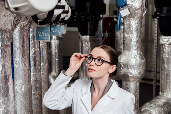 Attraktiver Ingenieur in weißem Mantel, der beim Anblick der Druckluftanlage eine Brille berührt — Stockfoto