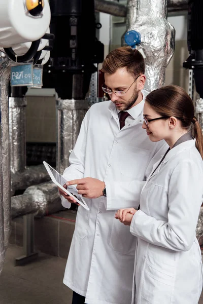 Handsome engineer pointing with finger at digital tablet near coworker and air compressor system — Stock Photo