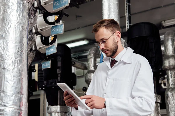 Bearded engineer in white coat pointing with finger at digital tablet near air supply system — Stock Photo