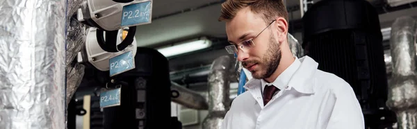 Panoramic shot of bearded engineer in white coat near air supply system — Stock Photo