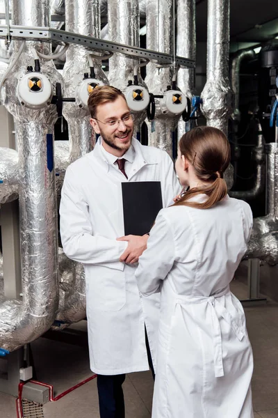 Cheerful engineer looking at coworker while standing near air compressor system — Stock Photo