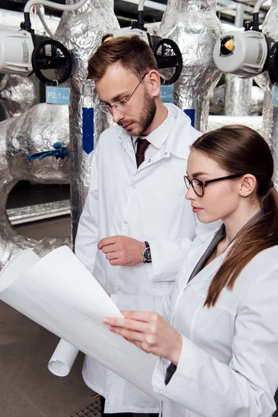 Ingenieros en batas blancas mirando el proyecto cerca del sistema de compresor de aire - foto de stock