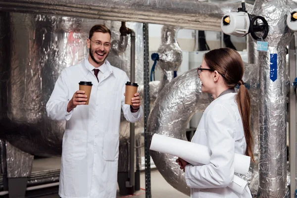 Ingénieur joyeux tenant des tasses en papier près de collègue heureux dans des lunettes — Photo de stock