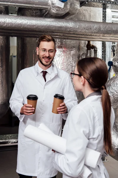 Счастливый инженер держит бумажные стаканчики рядом с коллегой в очках — стоковое фото