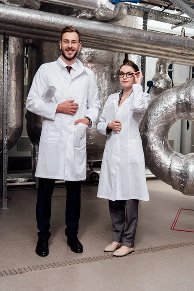 Cheerful scientist holding blueprints near beautiful coworker with digital tablet — Stock Photo