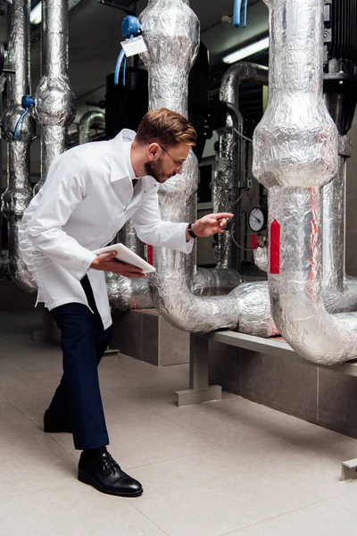 Ingénieur en manteau blanc tenant tablette numérique et pointant du doigt le système d'alimentation en air — Photo de stock