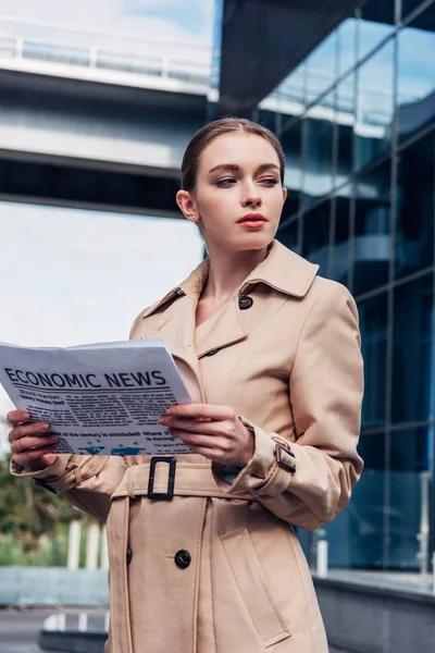 Приваблива жінка в траншеї пальто тримає газету зовні — стокове фото
