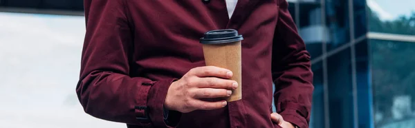 Panoramic shot of man in coat holding paper cup while standing with hand in pocket — Stock Photo