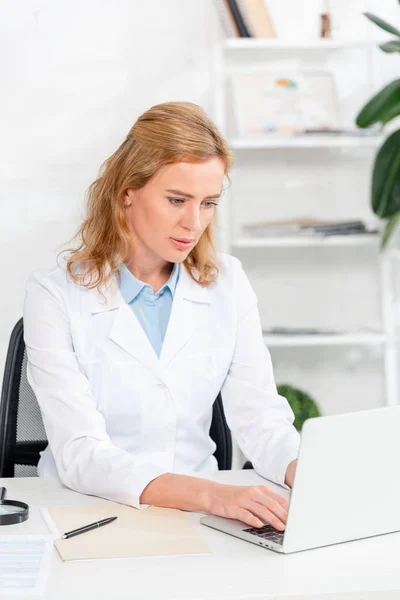 Nutritionniste attrayant assis à la table et en utilisant un ordinateur portable dans la clinique — Photo de stock