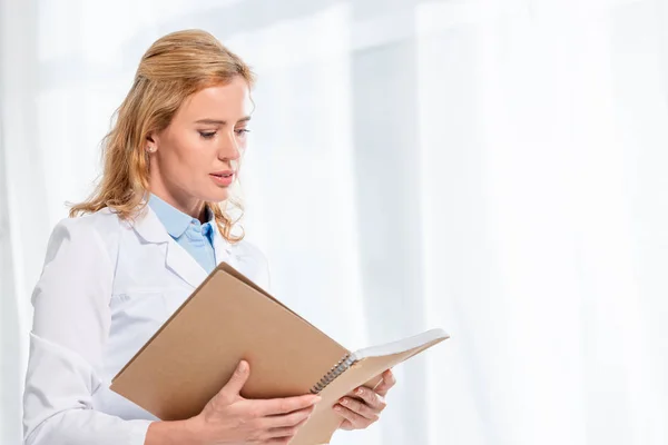 Attractive nutritionist holding and reading notebook in clinic — Stock Photo