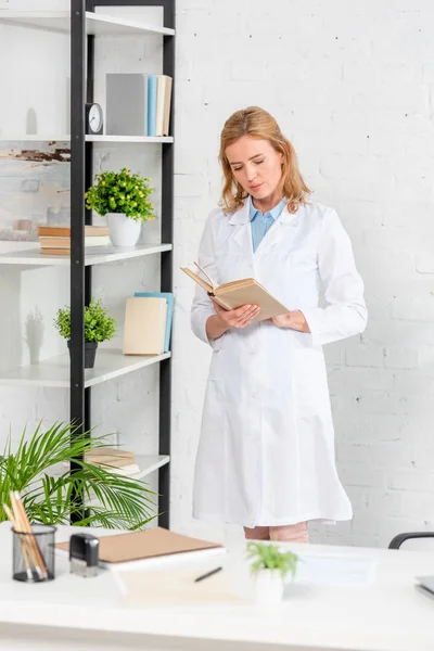 Atractivo nutricionista libro de lectura y de pie en la clínica - foto de stock