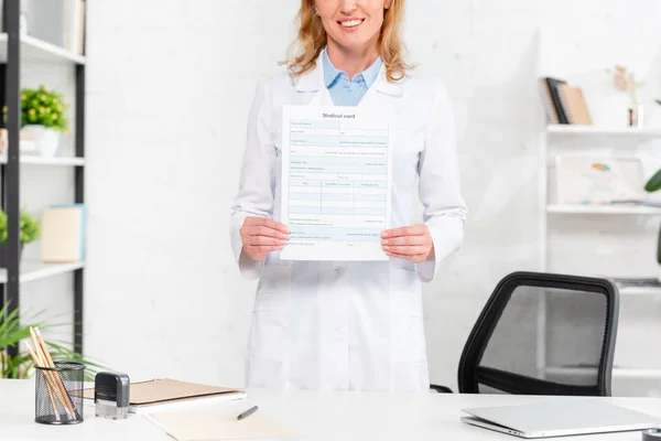 Vista recortada de nutricionista sonriente sosteniendo tarjeta médica en la clínica - foto de stock