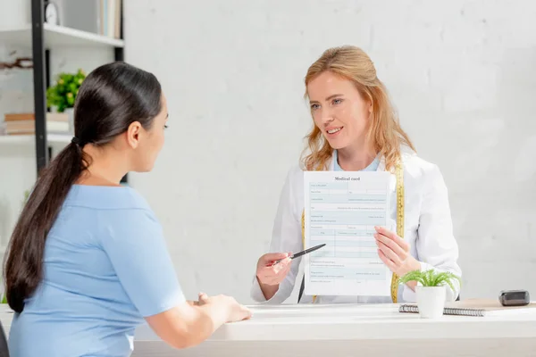 Atractivo nutricionista mostrando a paciente tarjeta médica en clínica - foto de stock