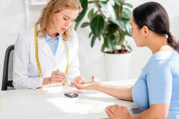 Attraktive Ernährungsberaterin sitzt am Tisch und nimmt Bluttest von Patientin in Klinik — Stockfoto