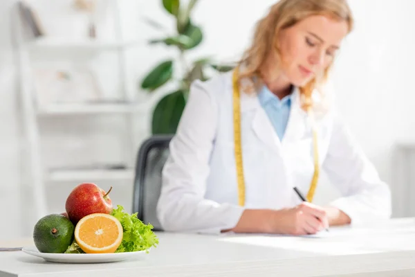 Selective focus of orange, avocado, lettuce and apple on plate — Stock Photo