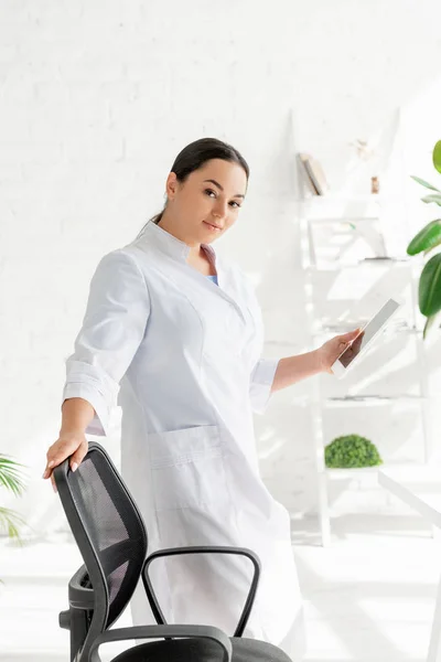 Attractive dermatologist holding digital tablet and looking at camera in clinic — Stock Photo