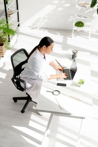 Blickwinkel auf attraktive Dermatologen, die am Tisch sitzen und Laptop in der Klinik benutzen — Stockfoto