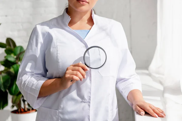 Vista ritagliata del dermatologo in possesso di lente d'ingrandimento in clinica — Foto stock