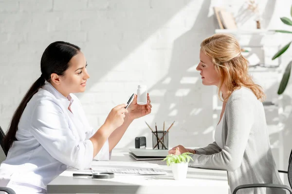 Side view of dermatologist showing bottle with pills to patient in clinic — Stock Photo