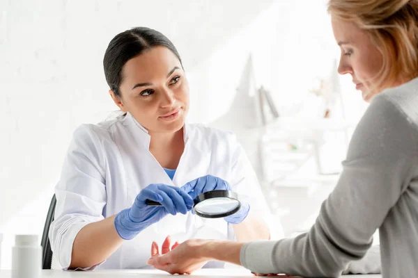 Dermatologist examining skin of patient with magnifying glass in clinic — Stock Photo