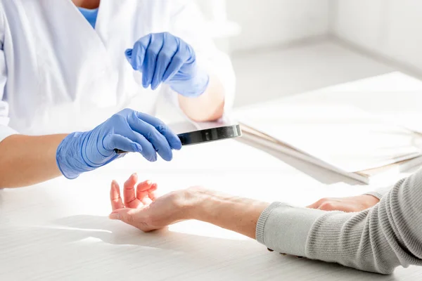 Vista recortada del dermatólogo examinando la piel del paciente con lupa en la clínica - foto de stock