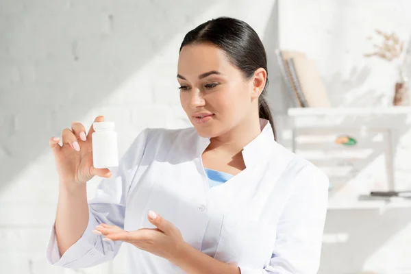 Attractive dermatologist in white coat holding bottle with pills in clinic — Stock Photo