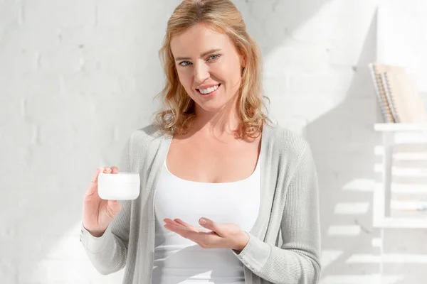 Femme souriante et attrayante pointant avec la main à la crème cosmétique — Photo de stock