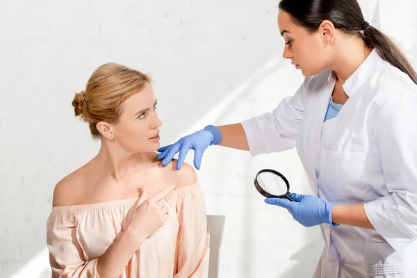 Dermatologist examining skin of patient with magnifying glass in clinic — Stock Photo