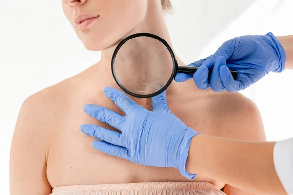 Vista recortada del dermatólogo examinando la piel del paciente con lupa en la clínica - foto de stock