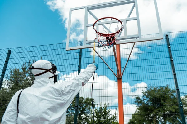 Cleaning specialist in hazmat suit and respirator disinfecting basketball court during coronavirus pandemic — Stock Photo