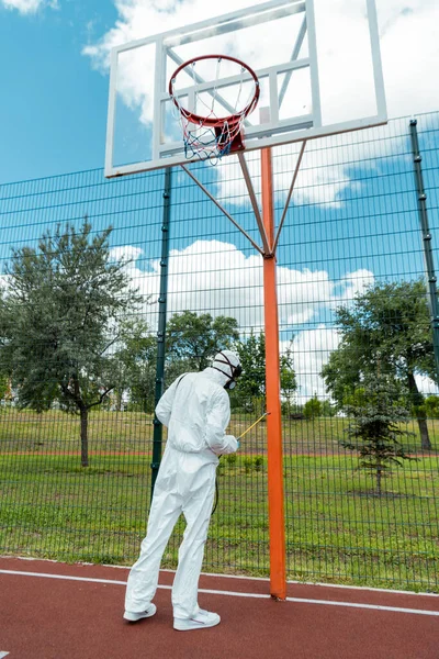 Cleaning specialist in hazmat suit and respirator disinfecting basketball court during coronavirus pandemic — Stock Photo