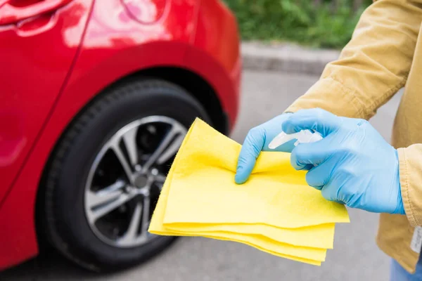 Partial view of man in medical gloves using antiseptic and rag for cleaning car during coronavirus pandemic — Stock Photo