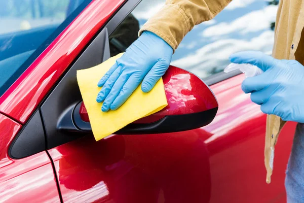 Cropped view of man in latex gloves using antiseptic and rag for cleaning car during coronavirus pandemic — Stock Photo