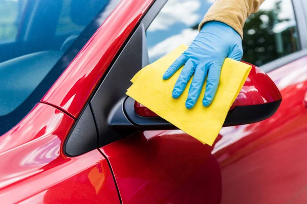 Vue recadrée de l'homme en gant de latex à l'aide de chiffon pour nettoyer la voiture pendant la pandémie de coronavirus — Photo de stock