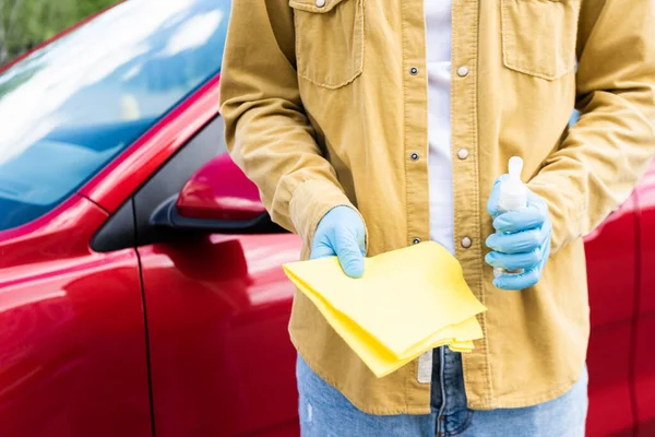 Cropped view of young man in latex gloves using antiseptic and rag for cleaning car during coronavirus pandemic — Stock Photo